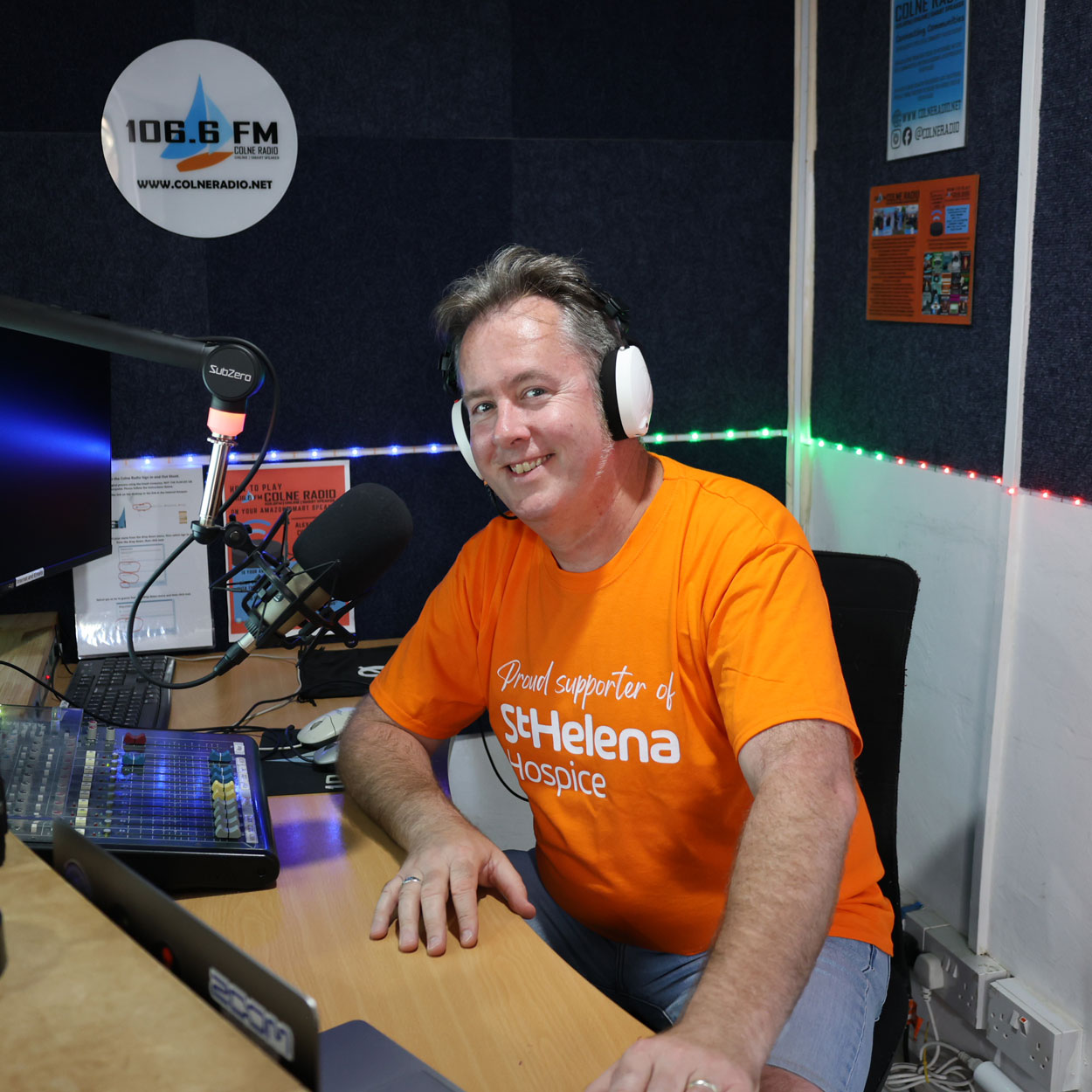 Rick Armstrong, hospice nurse, sitting at a radio desk wearing headphones in an orange St Helena Hospice tshirt