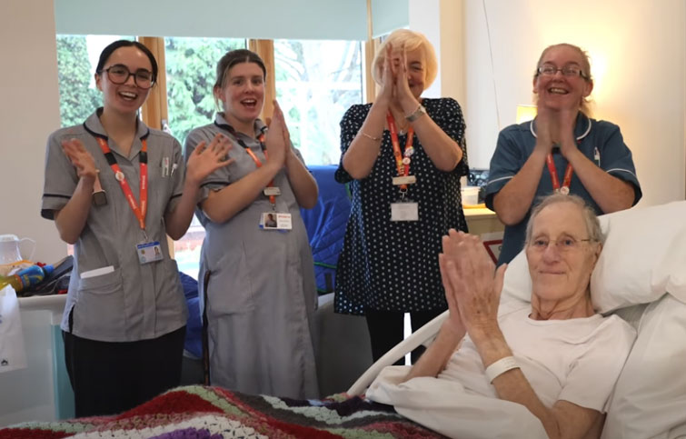 Ian in a bed at St Helena Hospice with nursing staff next to him all clapping